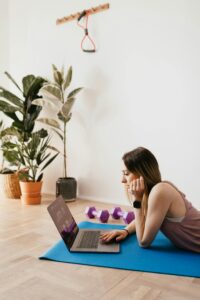 pexels-photo-4498454-4498454 Serious young female in activewear lying on blue yoga mat on floor and browsing laptop