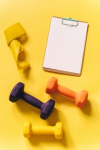 pexels-photo-8155161-8155161 Vibrant fitness gear including dumbbells and a clipboard on a yellow backdrop.